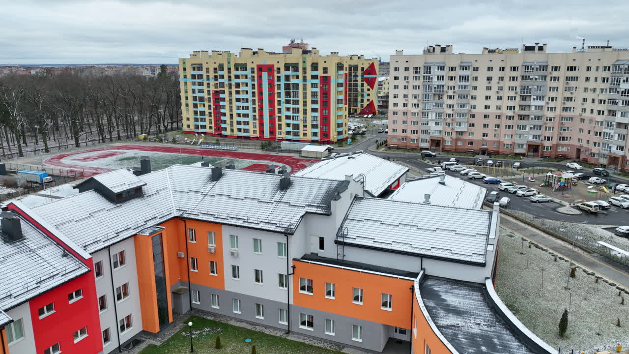 Unusual design of school building among the residential blocks of flats. Three-storied school premises surrounded by high houses and parked cars. Cityscape at the backdrop.