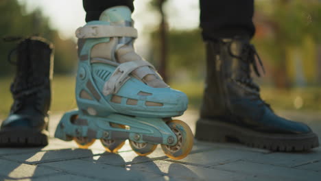 A close-up shot of a person wearing a light blue rollerblade on one foot, with the rollerblade wheels in motion on the ground, while the other foot remains in a black boot