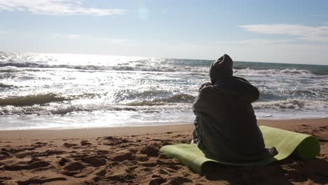 persona sentada en la playa, mirando el océano