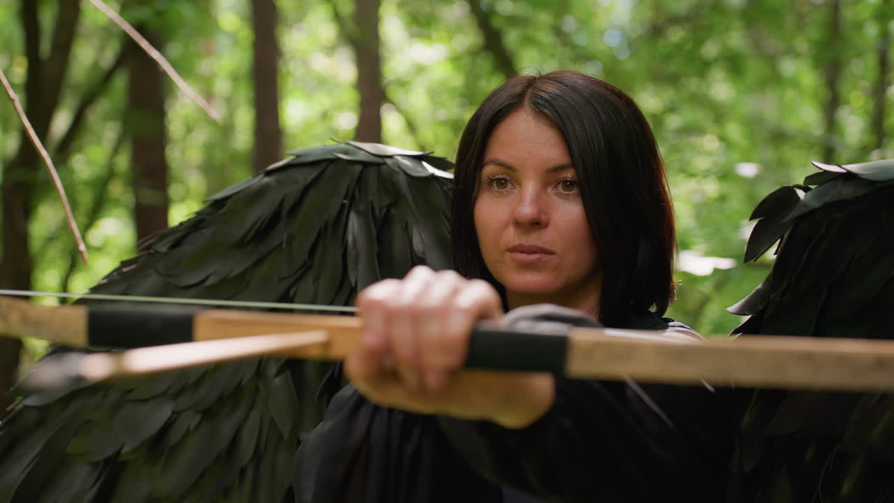 Close up of woman dressed as black fairy with large wings aiming bow in forest, eyes focused with gentle smile, sunlight flickering through leaves, magical fantasy moment filled with strength