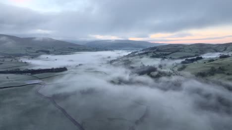 misty and foggy countryside valley with slow moving cloud static shot at dawn in winter including distant low mountains