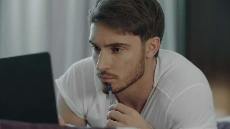 Persona pensante che guarda il computer a letto. Bello studente che utilizza l'istruzione online.