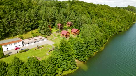 wooden cottage houses with red roofs for travelers accommodation in borucino forest near the lake, poland - pull back drone shot