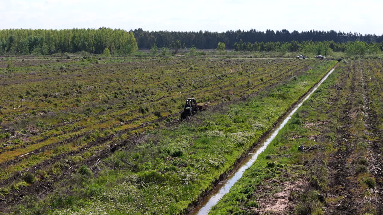 A tractor moves across a field during land preparation for reforestation on a clear and sunny day