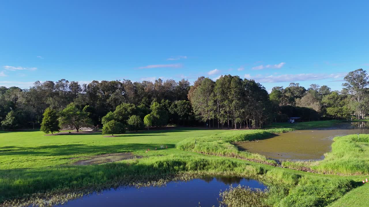 Drone footage captures lush greenery, wetlands, and a serene pond under clear blue skies in Gold Coast, Australia