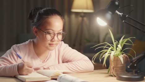 teenage girl doing homework at table in evening