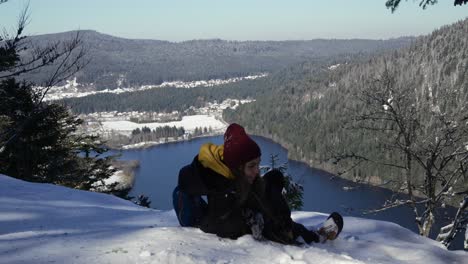 a young woman lays on the snow to relax after reaching the viewpoint over lake longemer in the vosges mountains