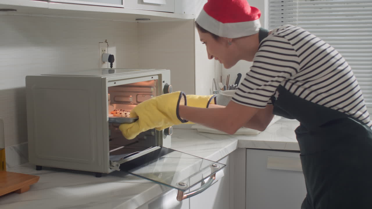 Donna con cappello natalizio che toglie i biscotti dal forno