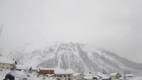 pan shot of snowy mountain side with village at bottom on a cloudy cold day