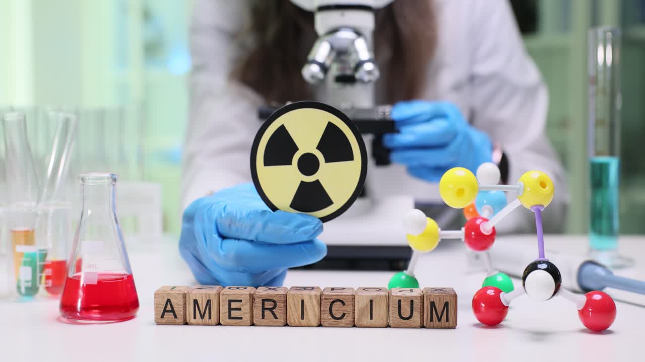Scientist in lab holding radiation symbol near Americium blocks and microscope