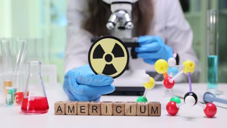 scientist in lab holding radiation symbol near americium blocks and microscope