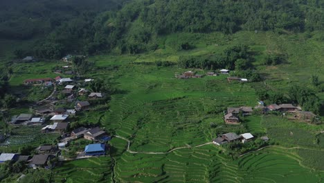 drone zoom in to green rice fields and village buildings nestled in the valley