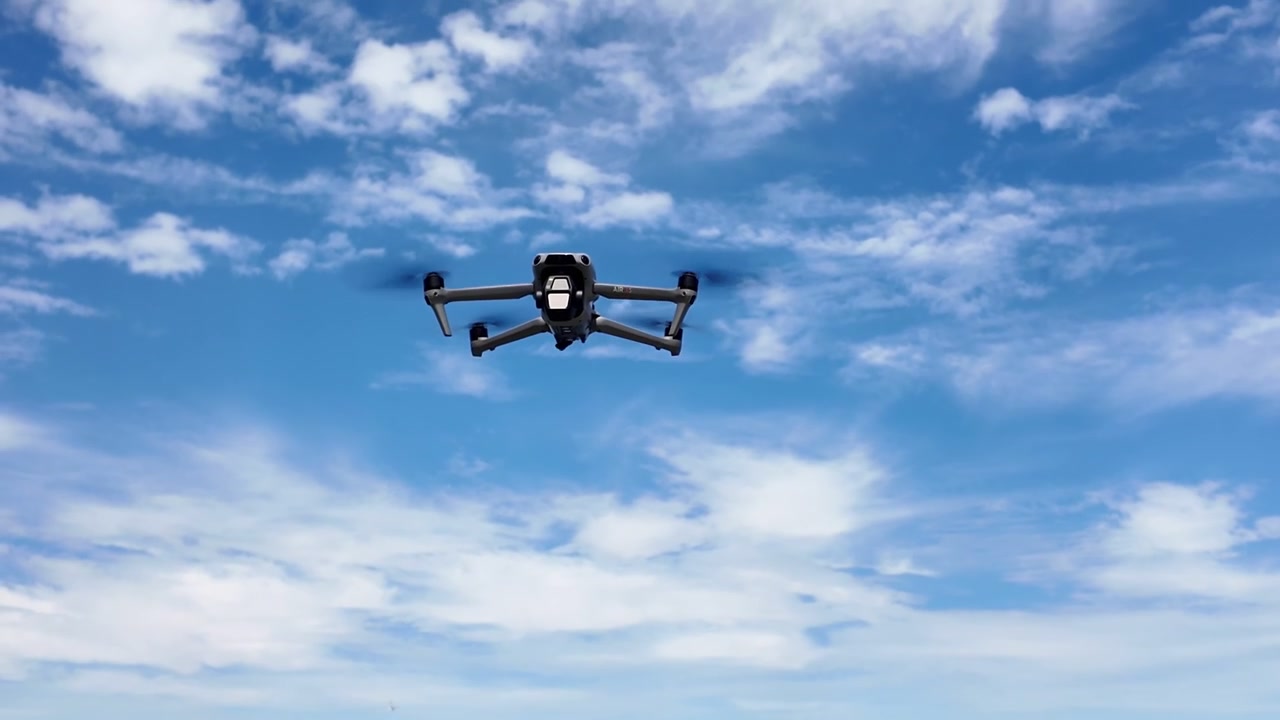 Moderno drone quadricottero per consumatori che sale dall'acqua verso il cielo blu con nuvole, utilizzando le sue eliche e la fotocamera per videografia aerea e operazioni di sorveglianza remota