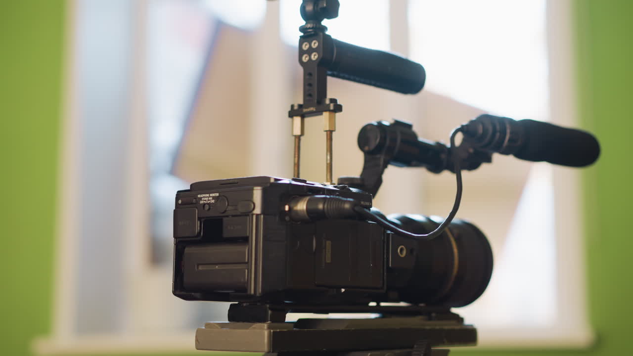 Close-up of hand adjusting camera on tripod head. Focus on tripod quick release plate and camera lens. Green wall in background with window light streaming through, creating soft highlights
