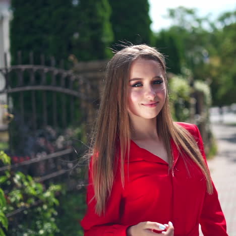 lovely girl in red dress. beautiful young model is standing outdoors and posing on camera. portrait of a pretty woman on the green trees background.