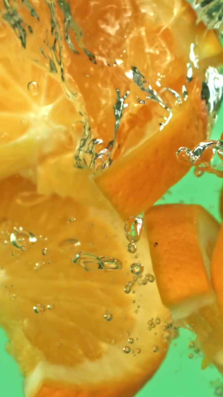 Fette d'arancia fresche che cadono nell'acqua con bolle su sfondo verde
