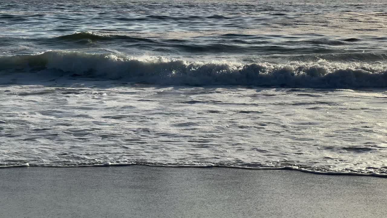 Little Waves break at the shoreline of Camps Bay Beach on a sunny evening. Camps Bay, Cape Town, South Africa.