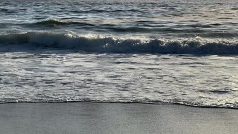little waves break at the shoreline of camps bay beach on a sunny evening. camps bay, cape town, south africa.