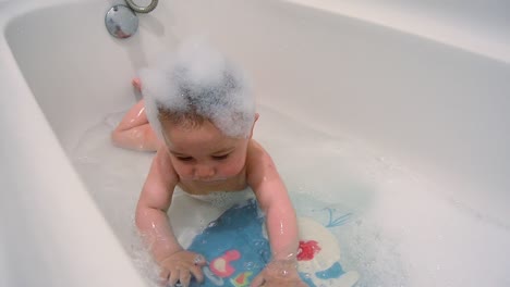 baby having foamy bath - cute six months old baby on his tummy in the bathtub