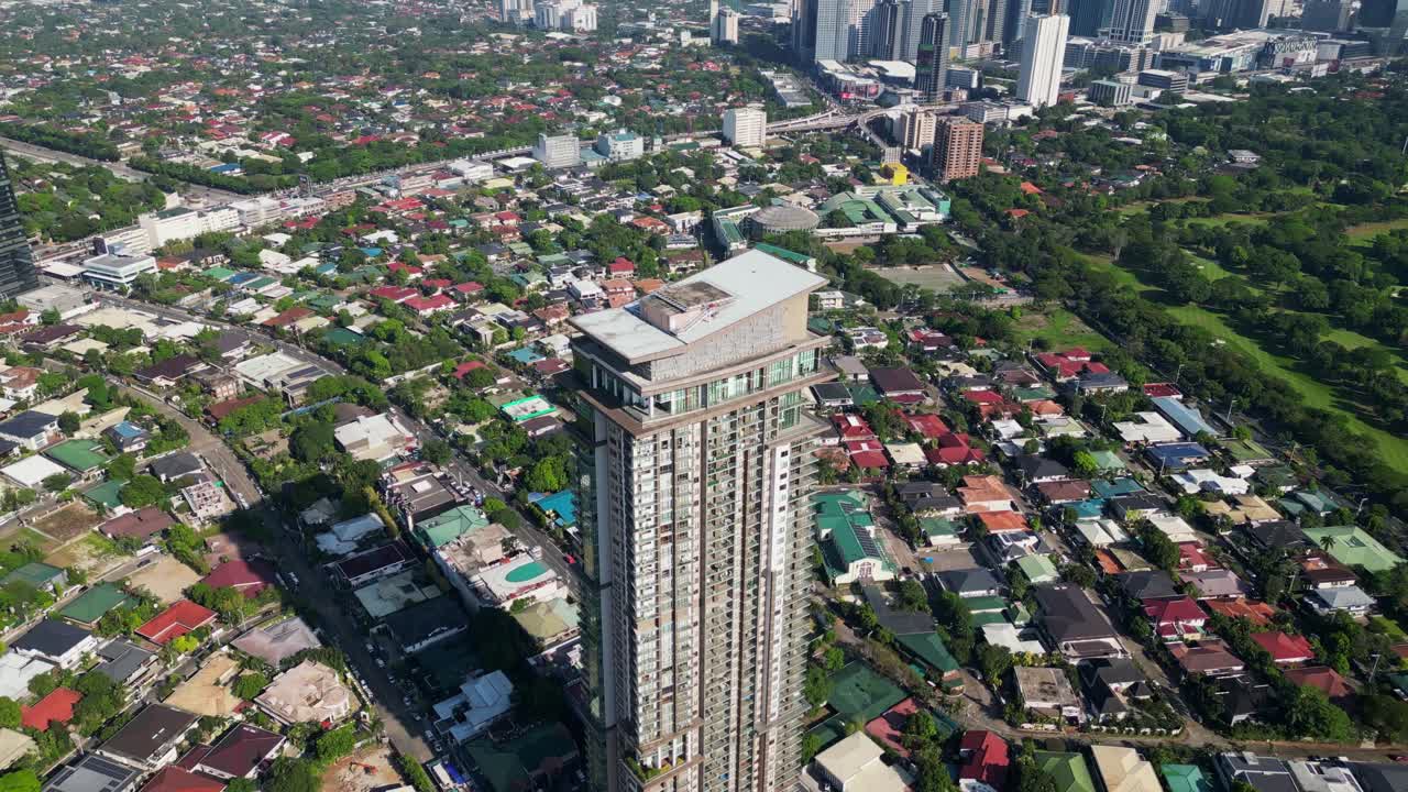Aerial pullback of residential condominium tower, Viridian in Greenhills, surrounded by homes and cityscape in San Juan City, Philippines.