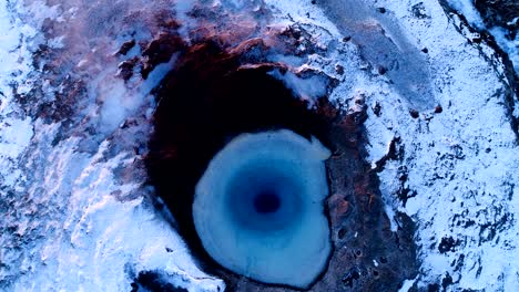 close-up view over the center of a geyser in geysir, iceland. smoke is getting out of the geyser with people walking all around the geyser, under the sunset.