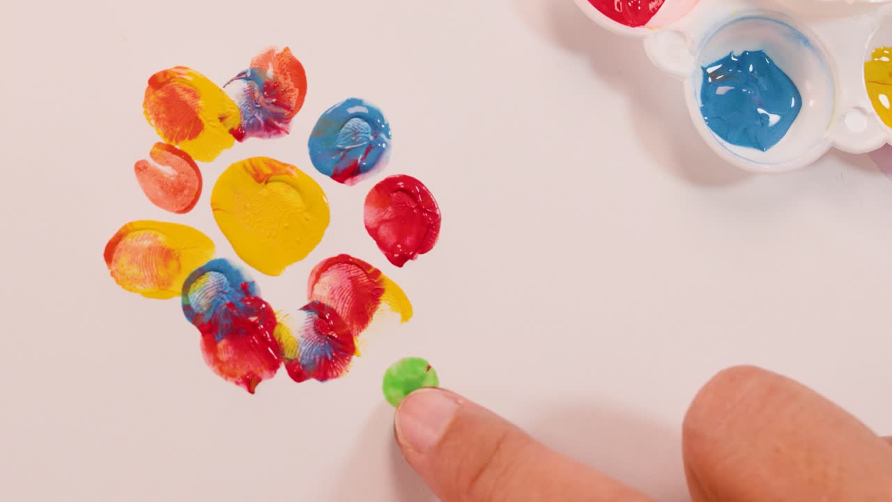 Hand creates a vibrant flower using finger paints, overhead view, bright lighting, steady camera