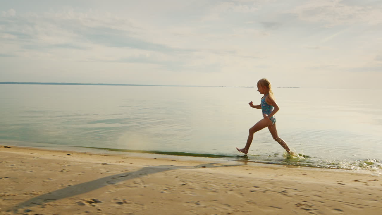 Ragazza divertente corre lungo la riva, i suoi piedi toccano l'acqua e si alzano molti schizzi, al rallentatore