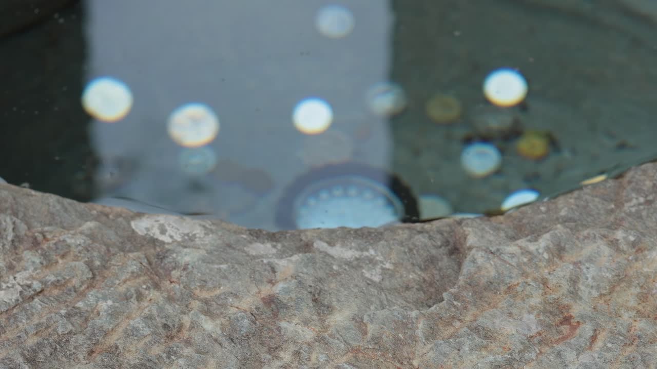 Close-up view of coins submerged in water within a stone basin, reflecting light.