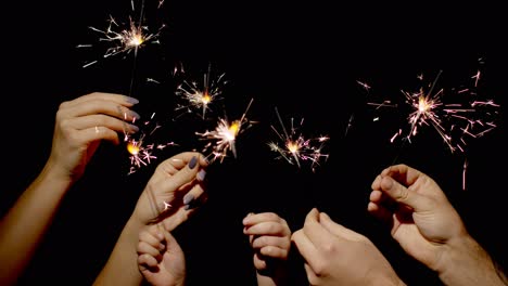 Close-up-of-hands-holding-and-waving-bengal-fire-burning-sparklers-in-front-of-black-background