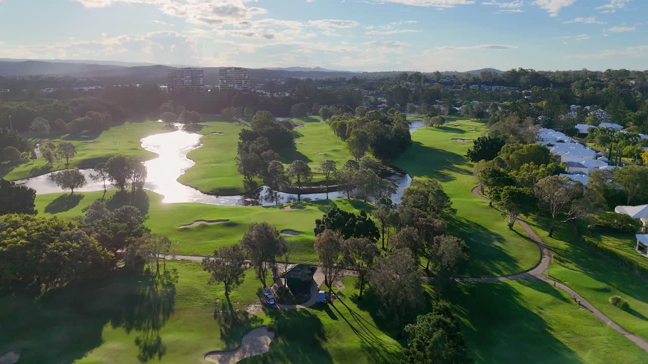 Drone footage captures a serene golf course and resort with lush greenery and winding water features under soft sunlight