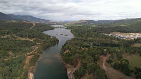Aerial-over-the-spillway-at-Lake-Eildon,-Victoria,-Australia-with-the-Goulburn-River-and-mountains-behind