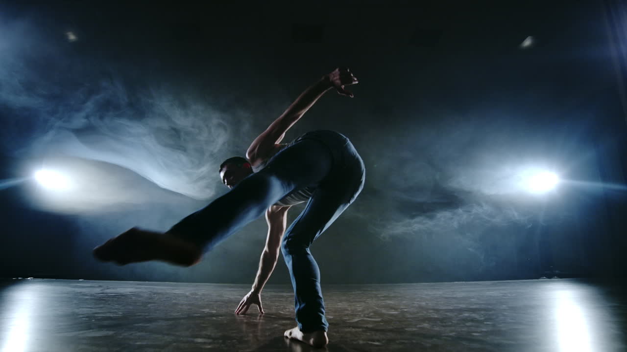 ballet moderno un hombre desde una posición sentada en el escenario salta salto mortal con rotación a la cámara en un escenario oscuro en el humo en el centro de atención. coreografía moderna en el escenario del teatro. espectáculo de danza.