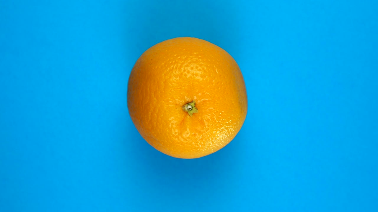 Frisk appelsin roterer på en farvet blå baggrund. Frugtjuicer, troper og afslapningskoncept