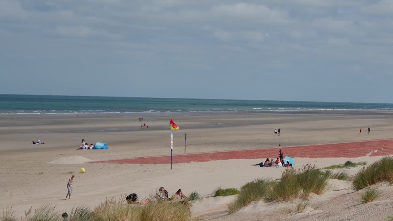 Groups and individuals enjoy leisure activities on a sunny, sandy beach with coastal dunes