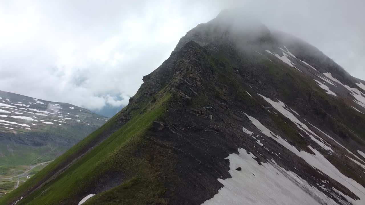 toma de drones de una montaña oscura, parcialmente cubierta de nieve y en las nubes