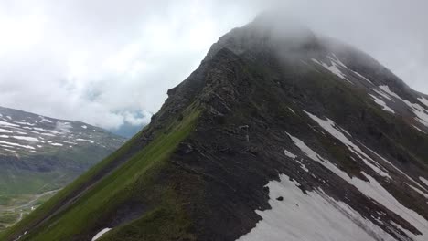 drone shot of a dark mountain, partially covered in snow and in the clouds