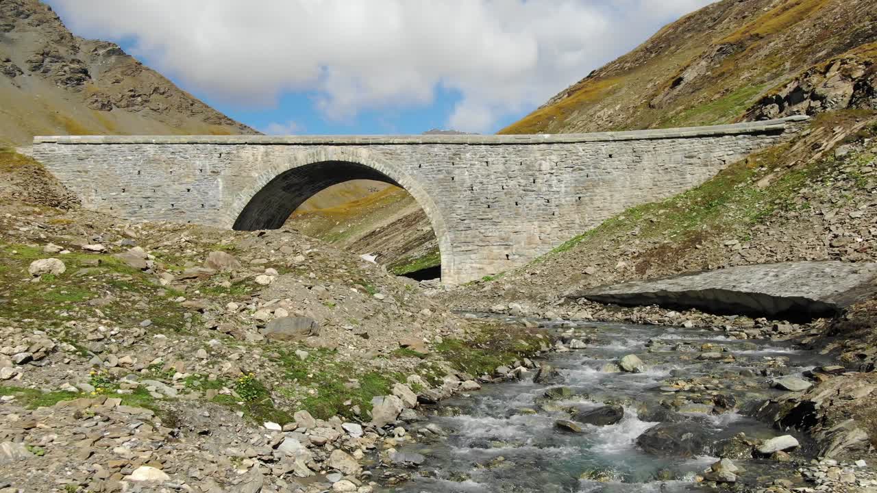 drone volando bajo sobre el arroyo con el puente de san carlos en el fondo, col de l'iseran en francia