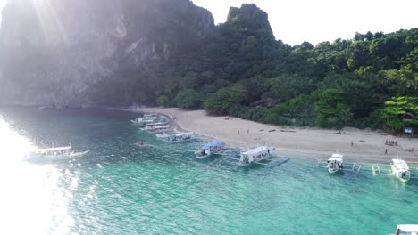 Vista-Aérea-Helicóptero-Isla-Tour-C-El-Nido---Palawan-:-Múltiples-Barcos-De-Gira-De-Banca-Anclados-En-Aguas-Turquesas-En-La-Playa-De-Arena-Blanca-Contra-La-Cabaña-De-Playa-Tropical