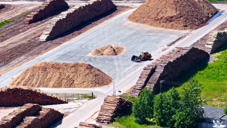 industrial timber yard at mērsrags port, latvia, showing a front loader working amongst huge stacks of logs and piles of wood chips for processing and export - aerial trucking