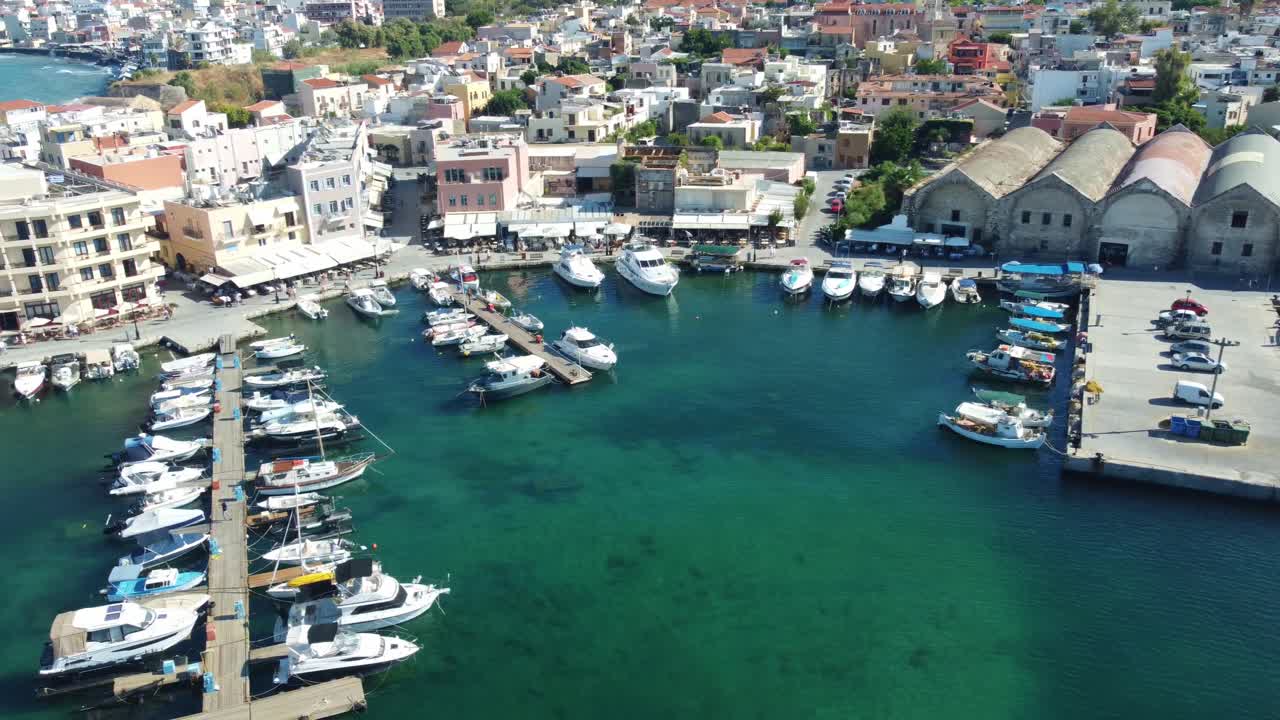 Aerial tracking left of Chania harbor with boats and buildings on a clear day in Crete, Greece