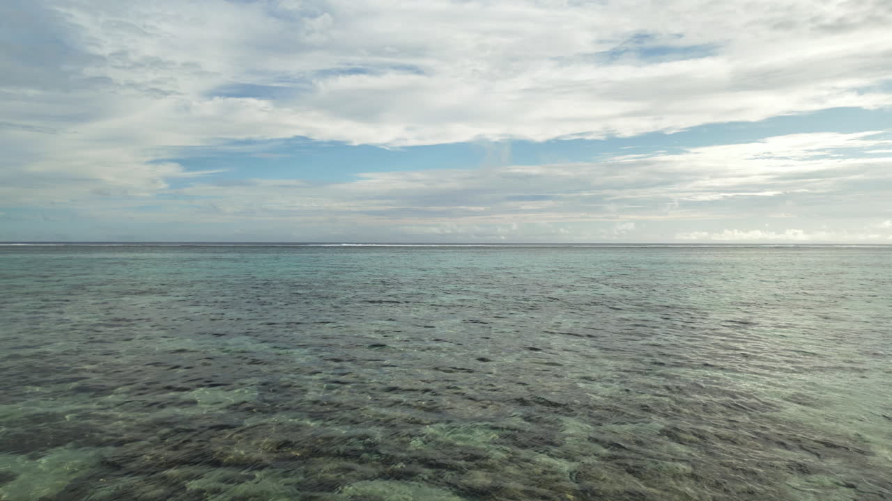 An endless view of a calm turquoise ocean under a bright cloudy sky, serene mood