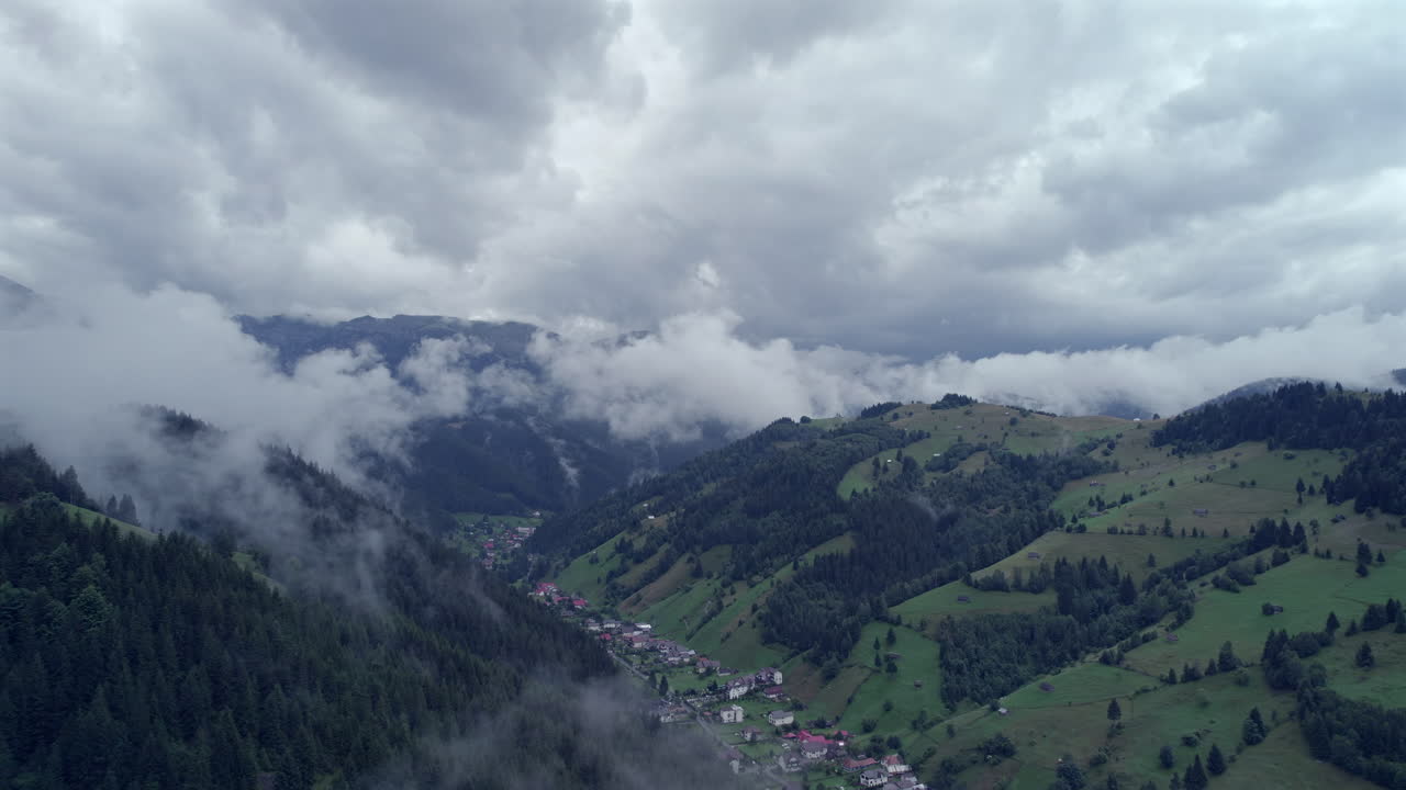 vista aérea que revela un valle con un pueblo turístico de montaña, altas montañas con bosques de abeto y nubes muy bajas