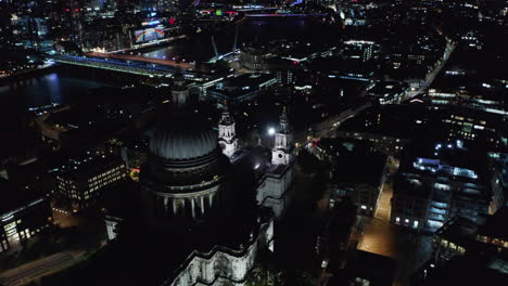 Aerial-view-of-famous-Saint-Pauls-Cathedral-at-night.-Slide-and-pan-shot.-Thames-river-and-illuminate-bridges-in-background.-London,-UK