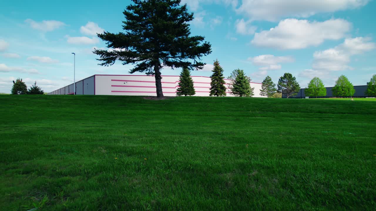 Low Forward Drone Shot Over Lush Grass Toward Industrial Building in North Wisconsin on a Sunny Day