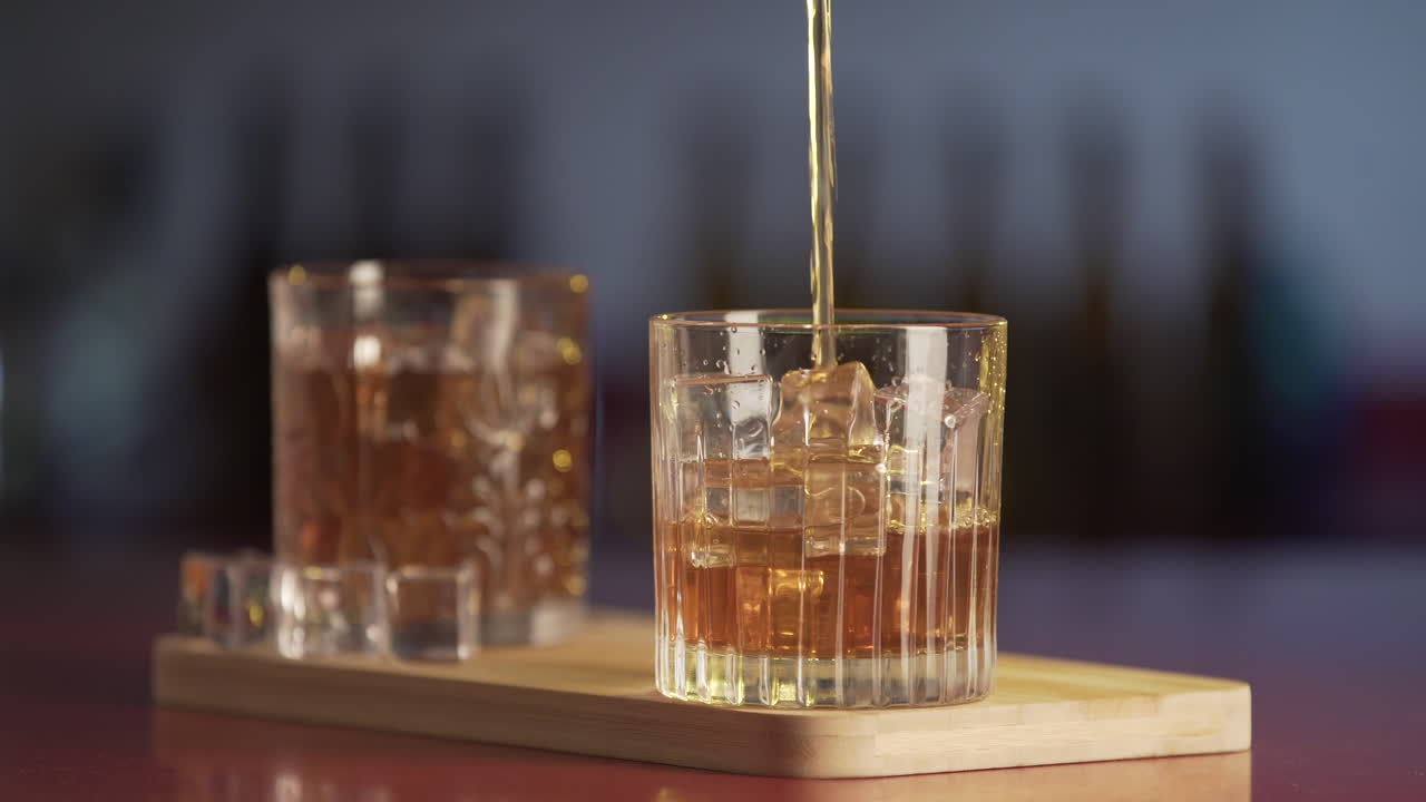 Whiskey poured in glass from bottle. Close-up of glass of whisky with ice cubes.