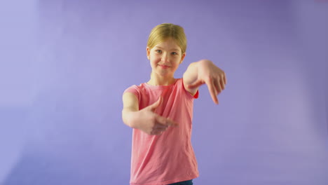 retrato de estudio de una niña sonriente haciendo la forma de un marco de imagen con las manos contra un fondo púrpura