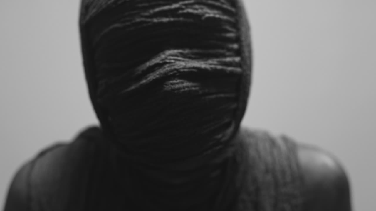 A mummy of a woman on a white backdrop looks into the camera