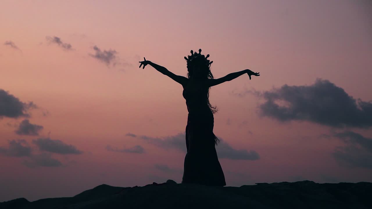 Silhouette of sexy, elegant and erotic arabian dancer performing belly dance moves on the beach during golden hour. Static. Slow motion