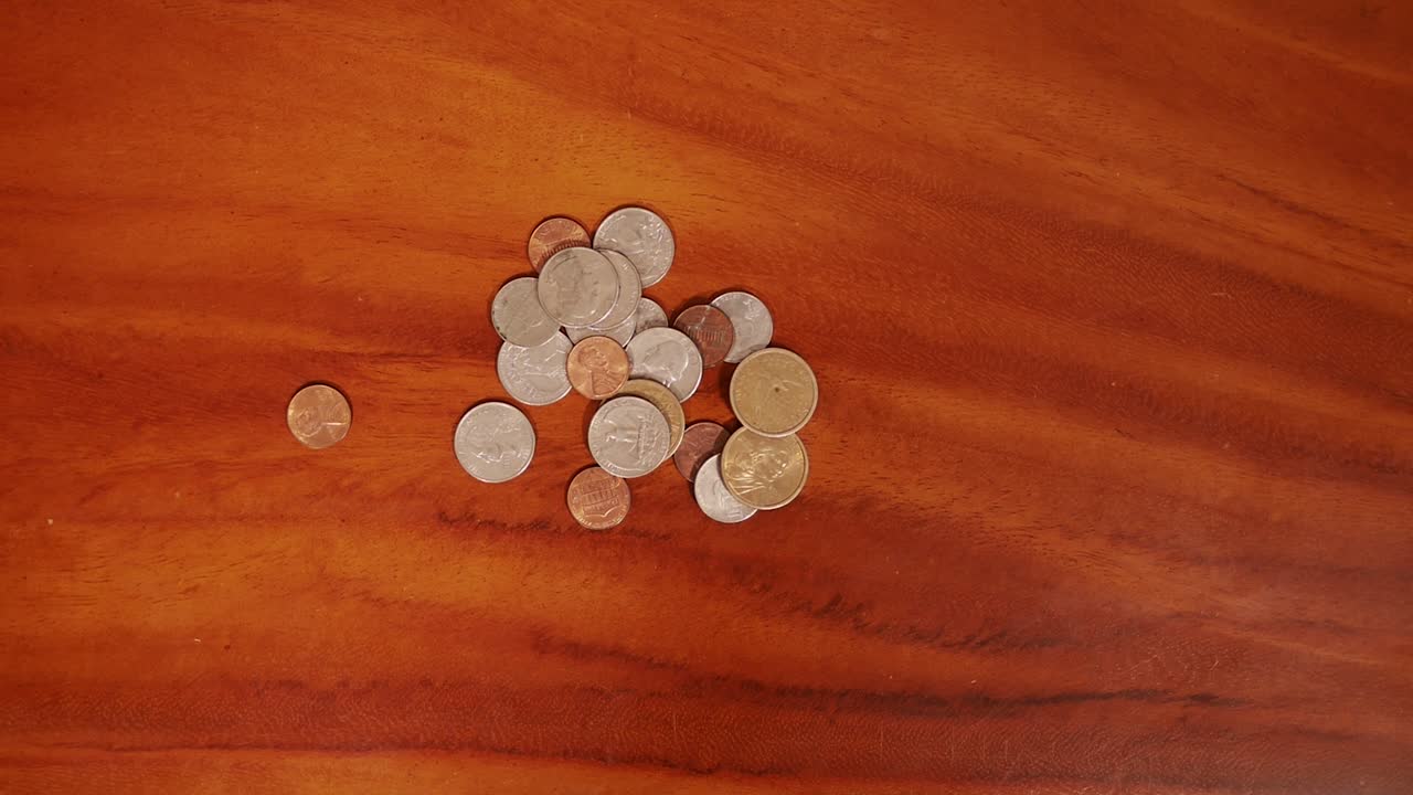 Overhead close up shot of male hand dropping United States coins on wood table