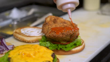 Squeeze-bottle-drizzles-red-sauce-on-fried-chicken-breast-sandwich,-close-up-slow-motion-slider-HD